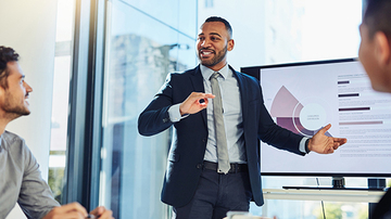 Man in front of screen speaking to colleagues